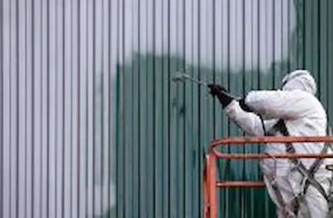 A professional painter using a spray machine to paint the exterior of a large commercial building, demonstrating Wilsonville Painters' expertise in commercial painting projects.
